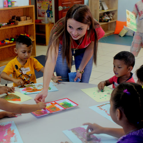 Fotografia de educadora explicando a 6 niños en una mesa